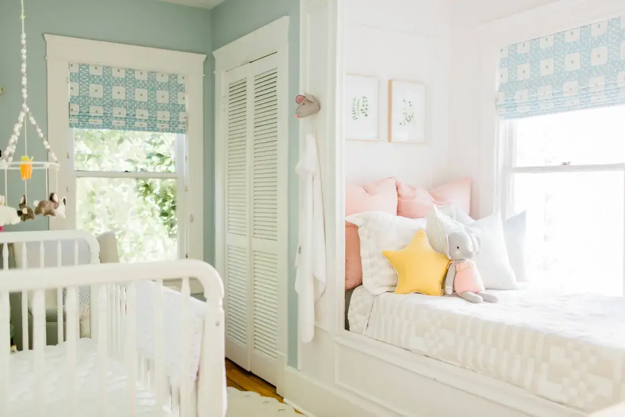 Sweet small nursery ideas for a girl, featuring a crib, a cozy window seat with plush toys, and charming decor.
