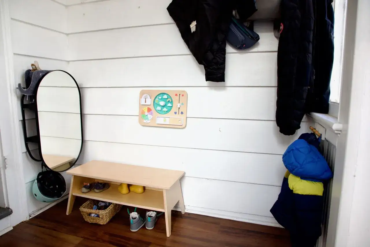 Montessori entryway ideas: a wooden bench with shoes, a weather chart, and coats hung neatly.