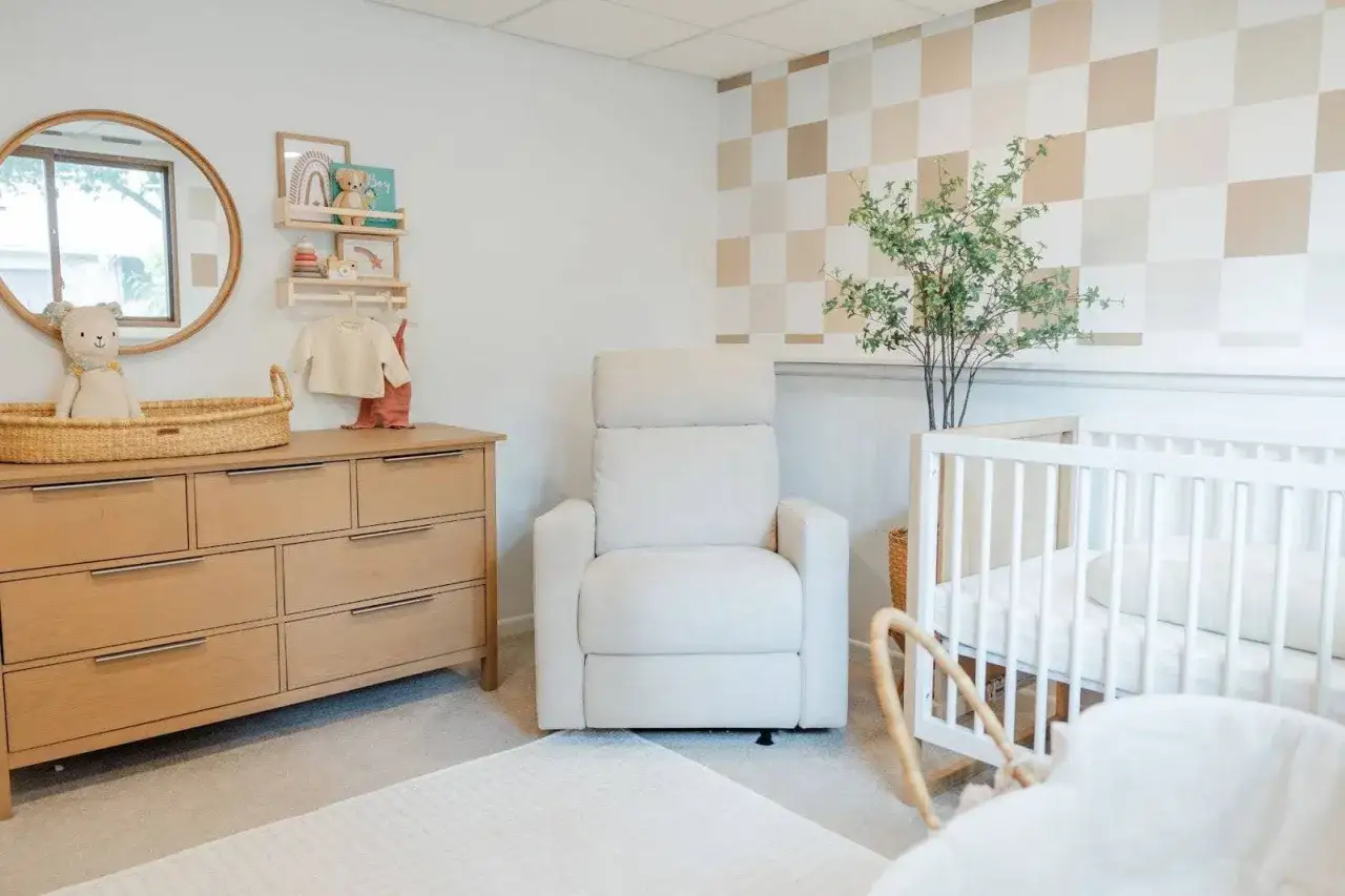 Cozy nursery with a white crib, plush recliner, and wooden dresser. Shelves above the dresser offer sweet crib decoration ideas with a teddy bear and rainbow art.