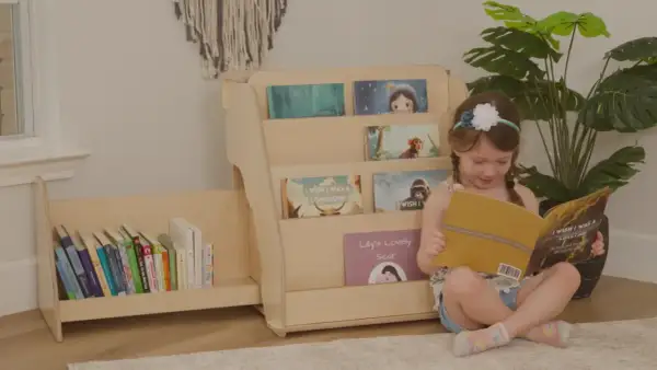 A young girl reads a book next to a DIY Montessori bookshelf filled with children's books.