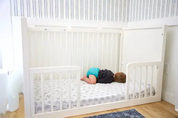 A baby sleeps on a floor bed with an elephant print sheet. This setup raises questions about whether floor beds are safe for babies.