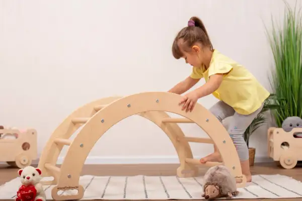A young girl in a yellow shirt climbs a wooden arch, showcasing gross motor activities.