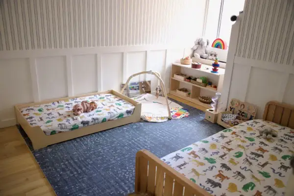 A baby sleeps on a low bed with animal print sheets, embodying the Montessori sleep on floor philosophy. Toys and a play mat are nearby.