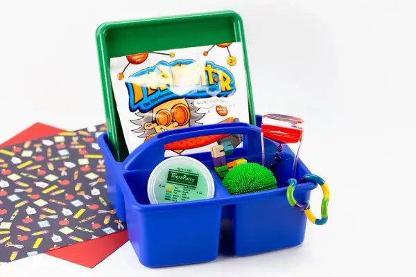 A blue caddy holds items for a sensory box: TheraPutty, a liquid timer, a spiky ball, and building blocks.
