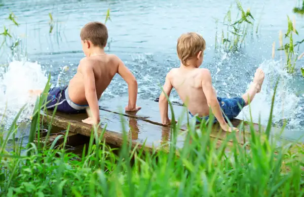 Two boys enjoy parallel play, splashing water from a wooden dock.