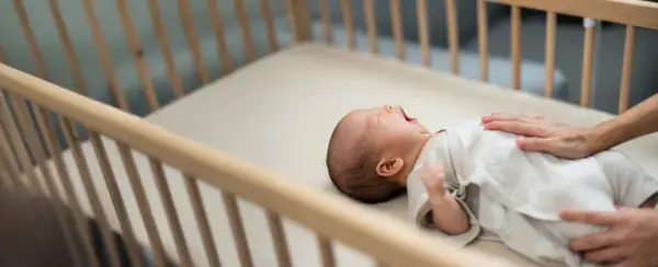 A baby yawns in a wooden crib. This image reassures parents that mini cribs are safe for their little ones.