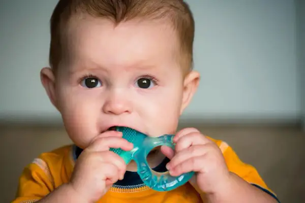 Baby chews on a blue teething ring, seeking relief. Does pacifier help with teething? This little one is finding comfort in a chew toy.
