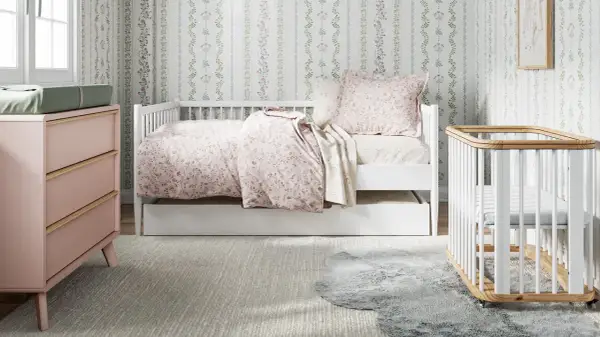 A charming small nursery features a white daybed with floral bedding, a pink dresser, and a white crib.