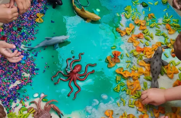 Ocean-themed sensory bin with toy sea creatures, colorful pebbles, and pasta provides engaging sensory activities for 1 year olds.