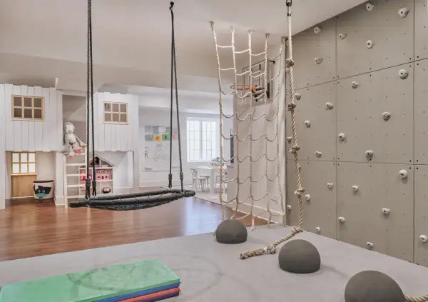 A child's indoor adventure zone with a climbing wall, net, and swing, embodying a Montessori aesthetic.