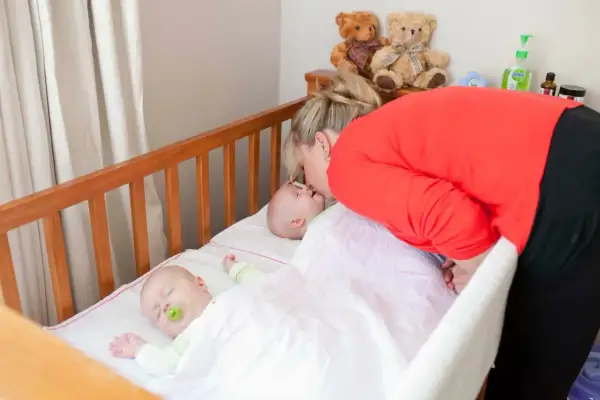 A mother kisses her baby in one of two **double baby cribs**. Another baby sleeps peacefully nearby.
