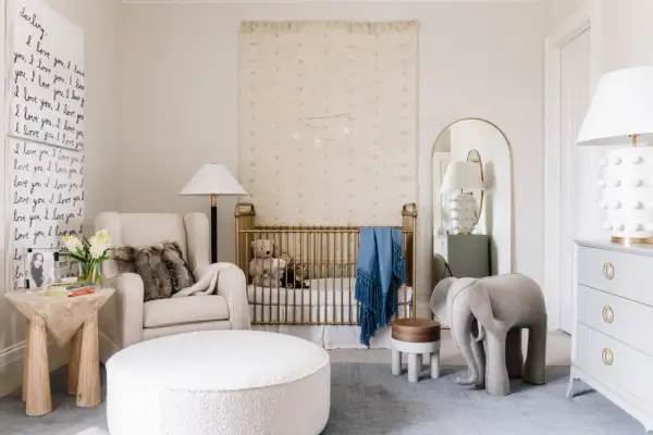 A serene nursery with a gold crib, plush armchair, and elephant stool. This space offers fun nursery ideas with its whimsical decor and cozy atmosphere.