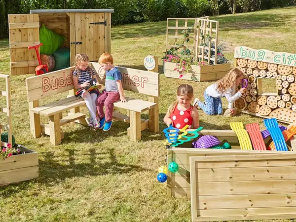Children explore a vibrant Montessori garden, discovering nature's wonders. A bug city invites curiosity, while a planter box bursts with colorful blooms.
