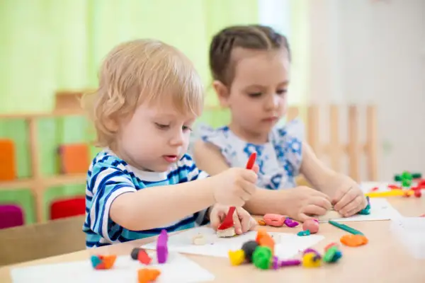 Two children engage in parallel play vs associative play, molding colorful clay at a table.
