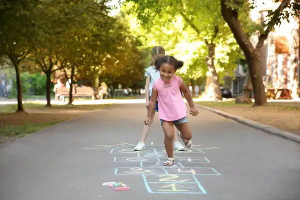 Kids learn shapes like squares and rectangles when playing hopscotch. Two girls are playing hopscotch on a sunny day.