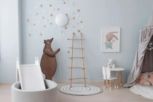 A whimsical nursery room, perfect for learning how to paint a nursery room. A bear holds a balloon, stars adorn the walls, and a bunny picture hangs above a small table.