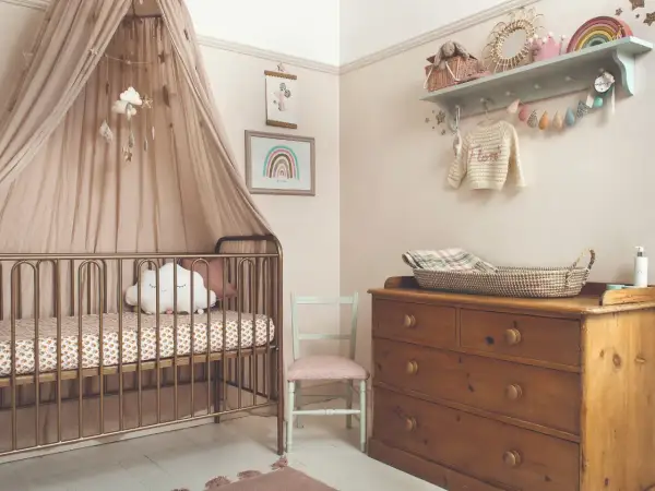 Dreamy small nursery ideas for a girl, featuring a gold crib with a cloud pillow, a rainbow print, and a vintage dresser.