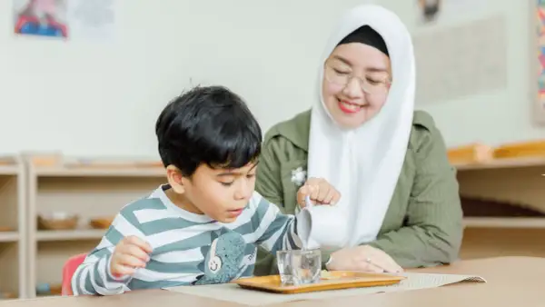 A child practices pouring water in a Montessori classroom, learning practical life skills inspired by nature.