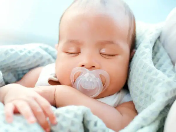 A peaceful newborn sleeps soundly, a pacifier in their mouth. This image shows that newborns do use pacifiers for comfort.