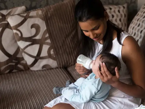 A mother gently feeds her baby from a bottle, holding him in a comfortable, paced feeding position on her lap.