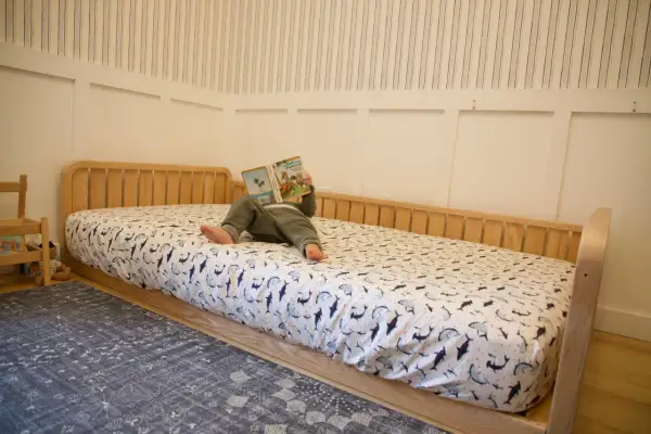 A child reads a book on a DIY Montessori bed with shark-patterned sheets.