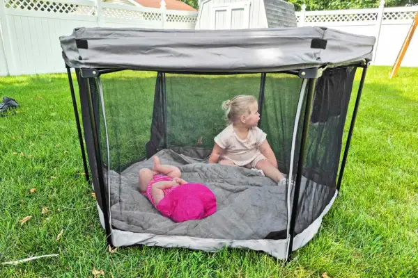 Two toddlers play in a portable playpen, a safe space often called a baby bed.