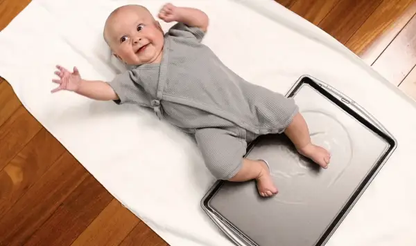 Joyful baby giggles during water play, kicking tiny feet in a shallow pan.