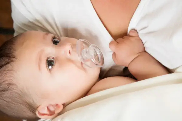 A baby with a pacifier, nestled close to their mother's chest, perhaps after breastfeeding.