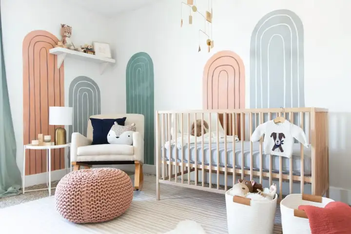 A modern nursery with rainbow wall art, a crib, and a comfy chair. Perfect for twin nursery themes with its neutral colors and playful design.